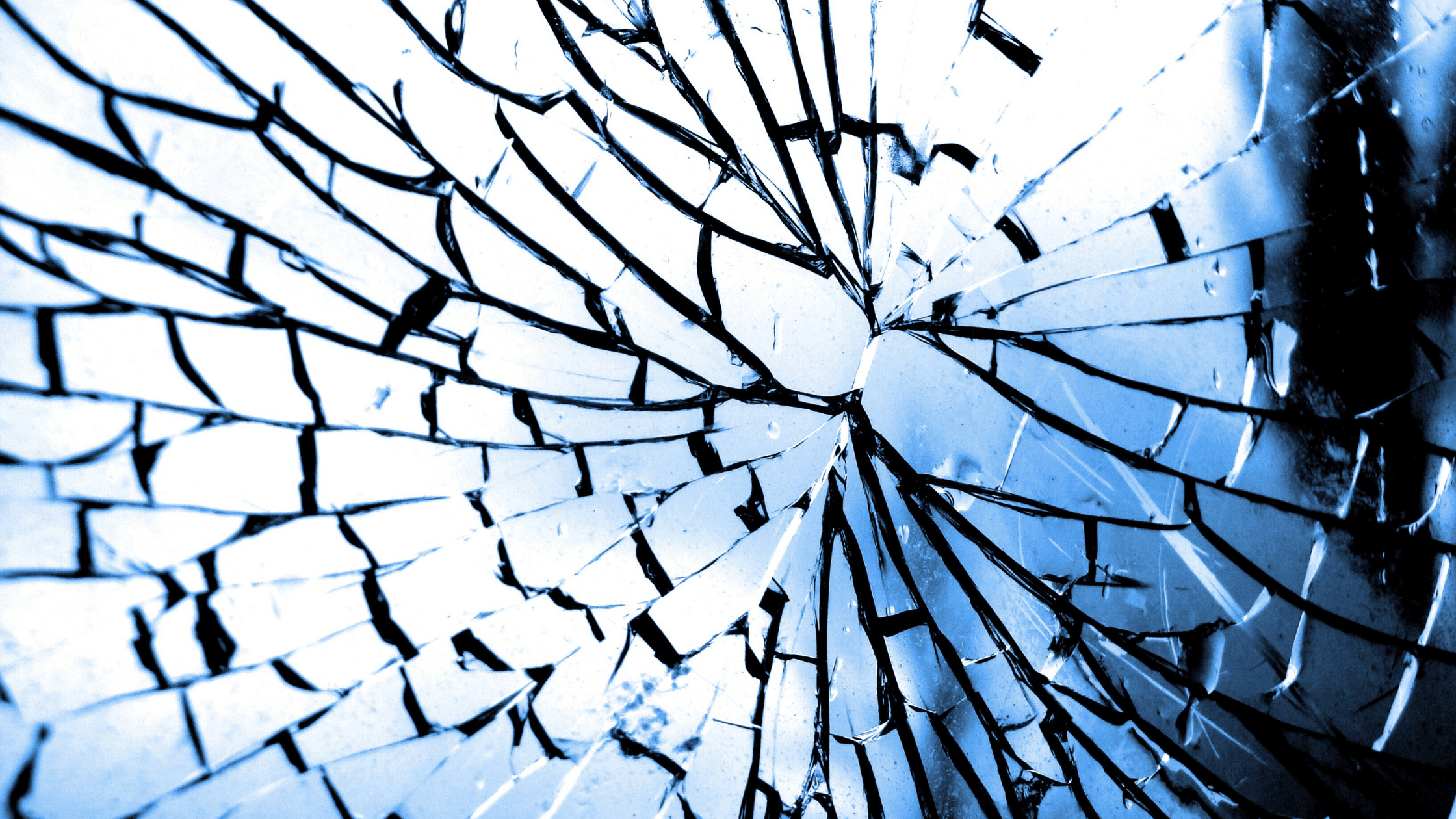 Close-up of shattered glass with a radial pattern, tinted in blue, creating a striking, abstract visual effect.