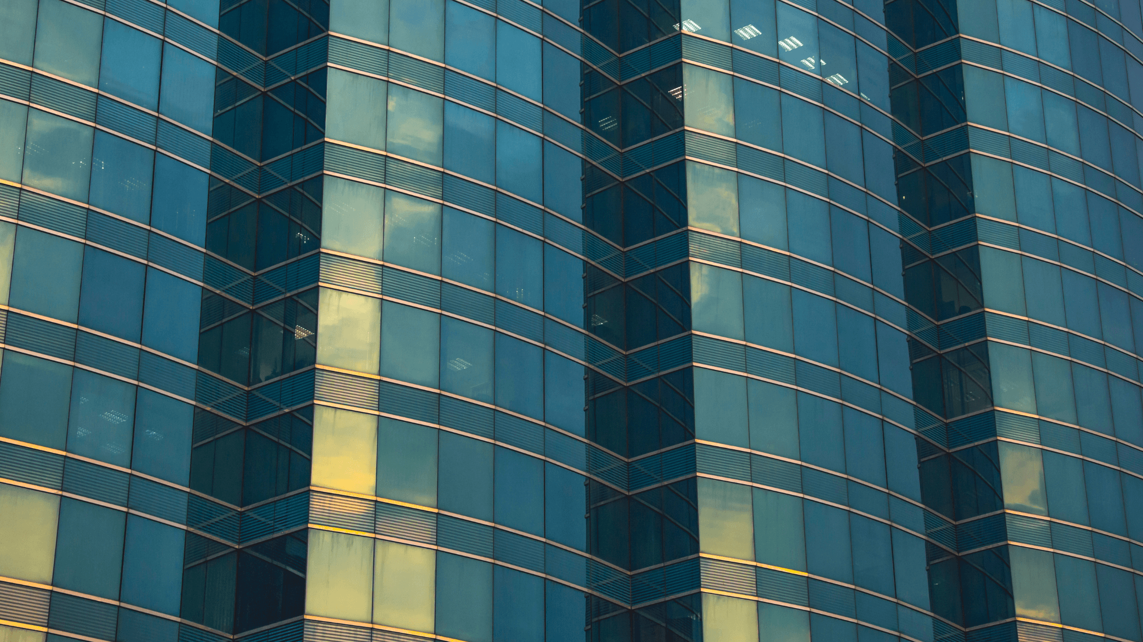 Close-up of a modern glass building facade with reflective blue-tinted windows highlighting geometric lines and subtle reflections of the sky.