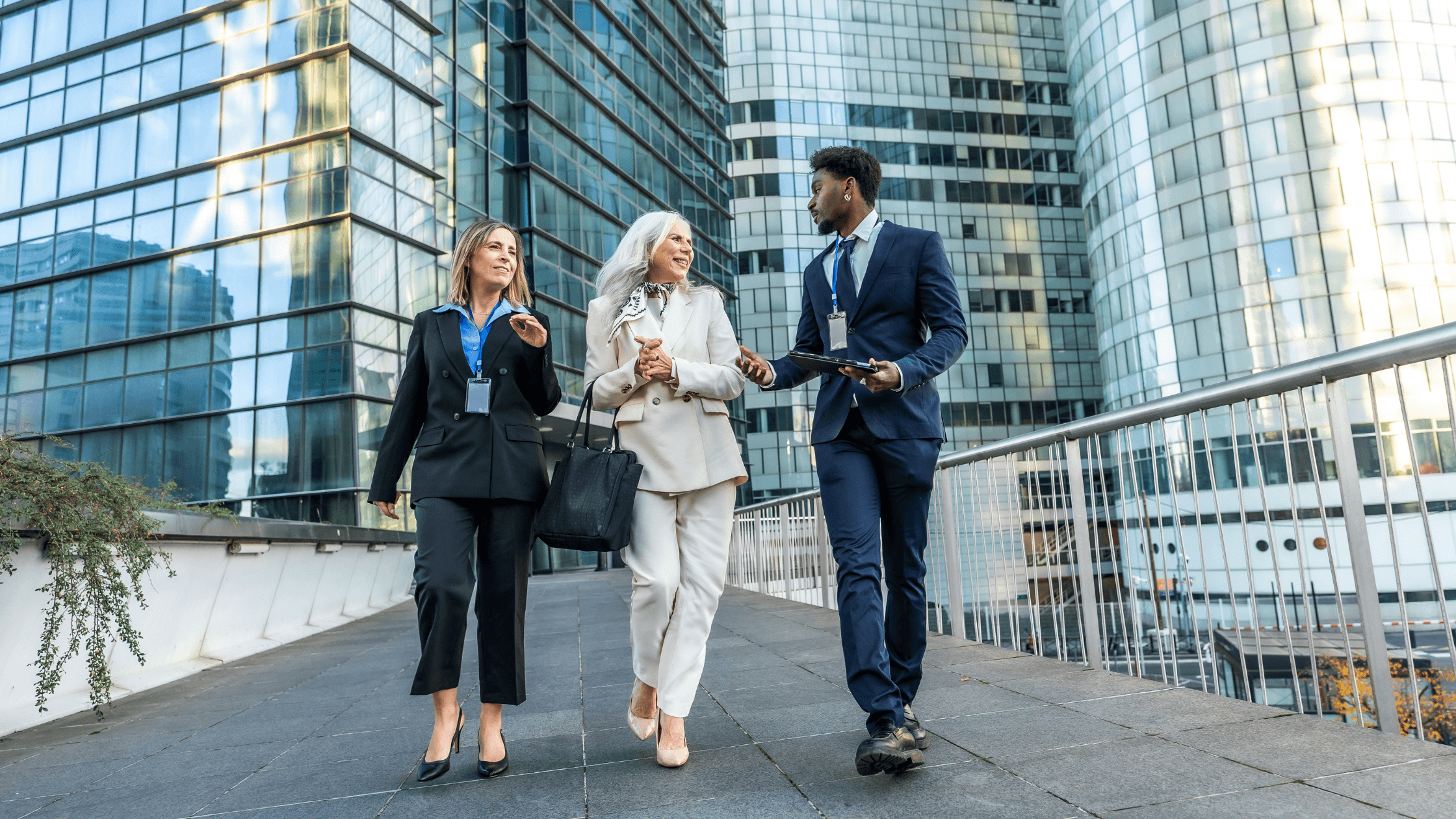 Three business professionals walk together, conversing outdoors near modern glass buildings.