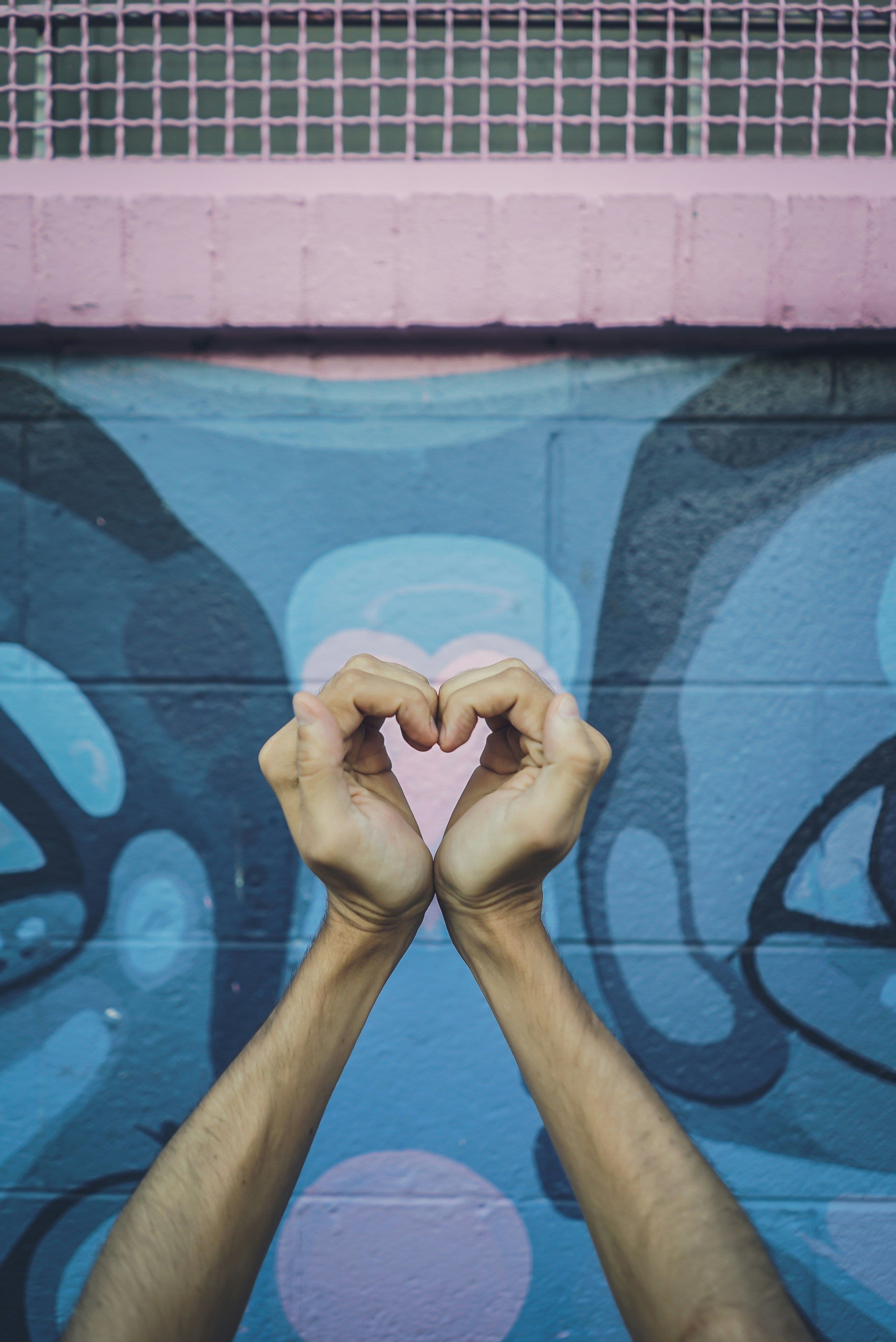 Hands forming a heart shape against a colorful mural with abstract blue and pink designs.