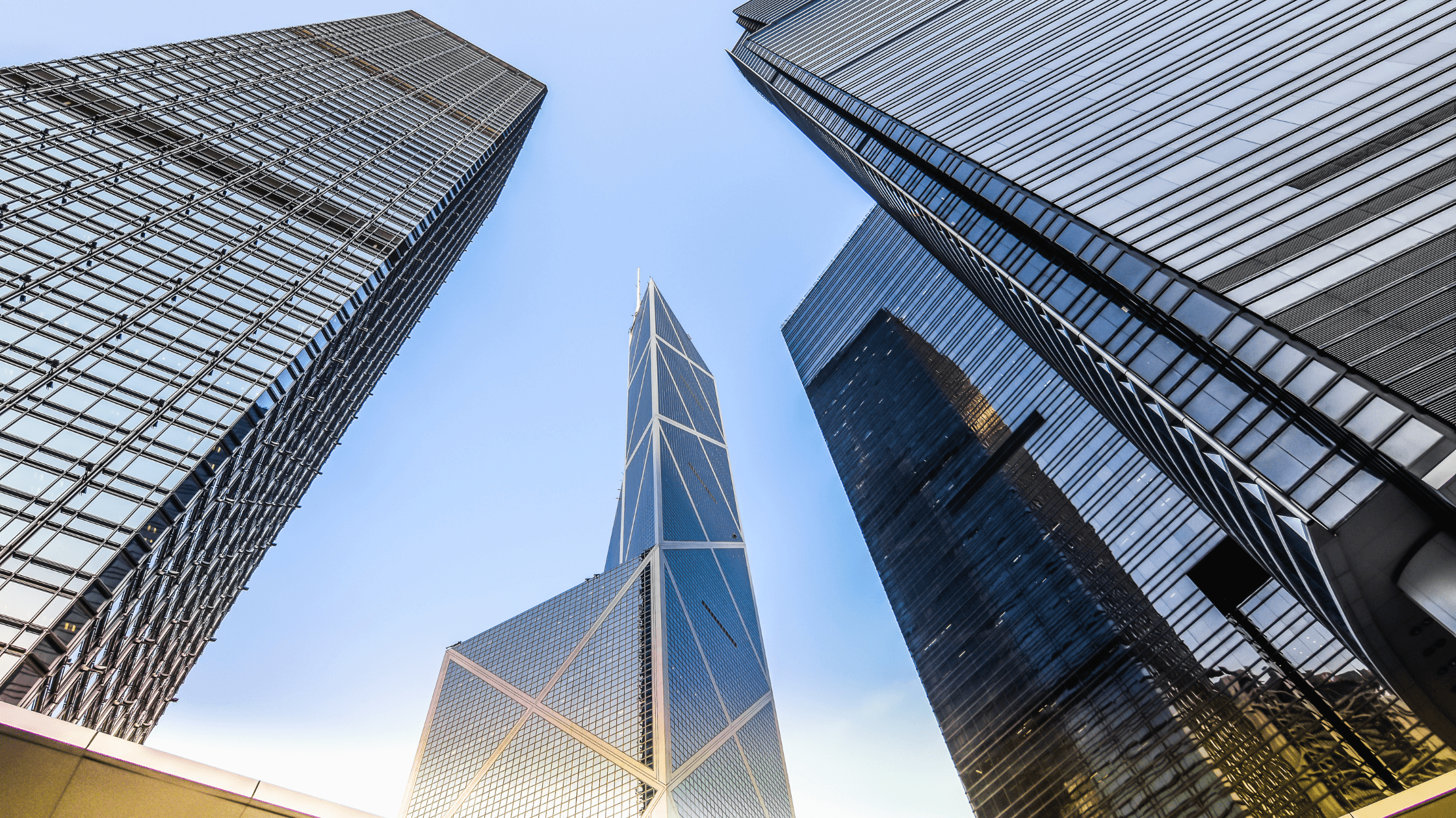 Upward view of four modern skyscrapers with reflective glass facades against a clear blue sky.