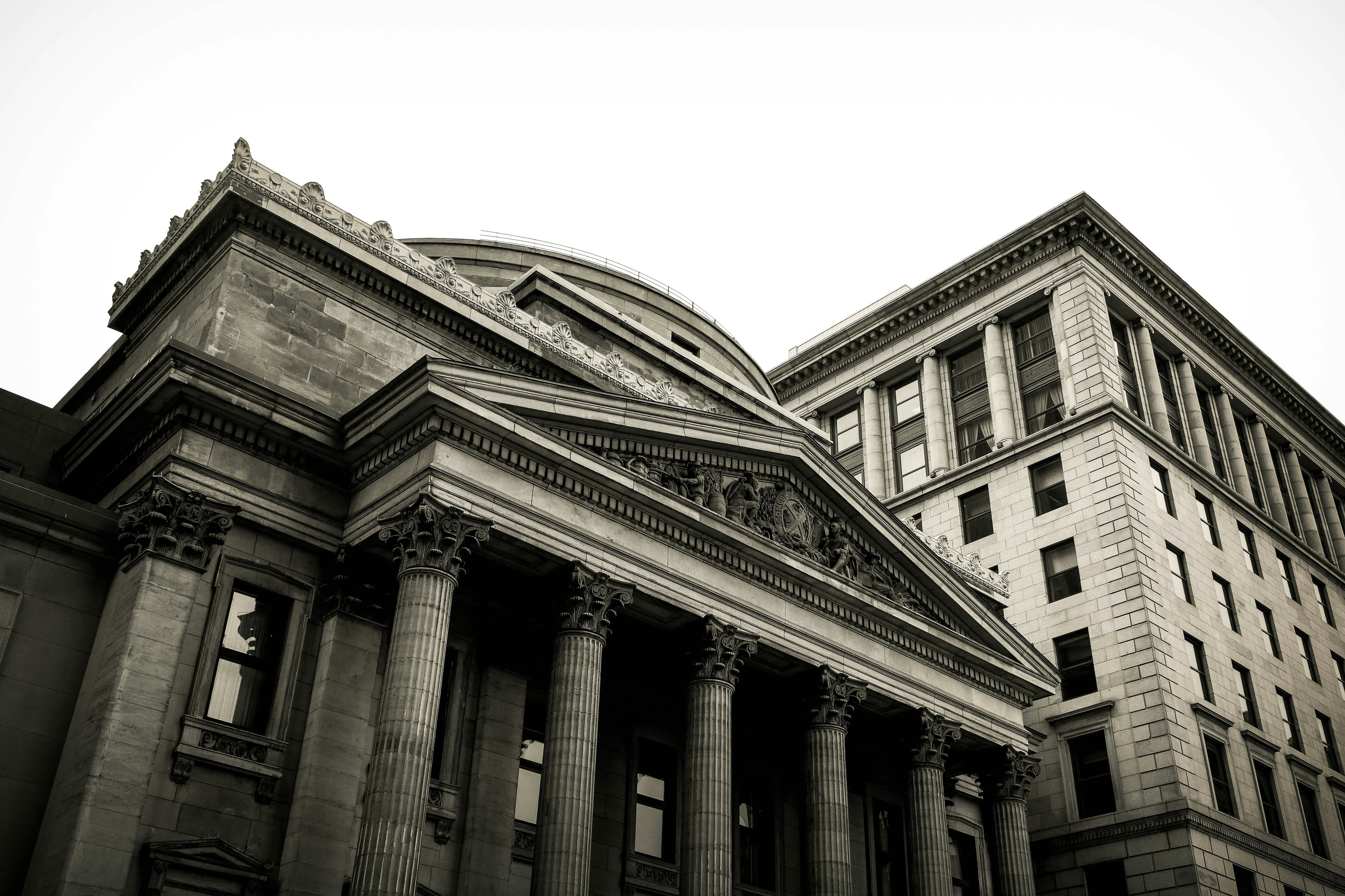Black and white image of a neoclassical building with columns and ornate facade, next to a high-rise with symmetrical windows.