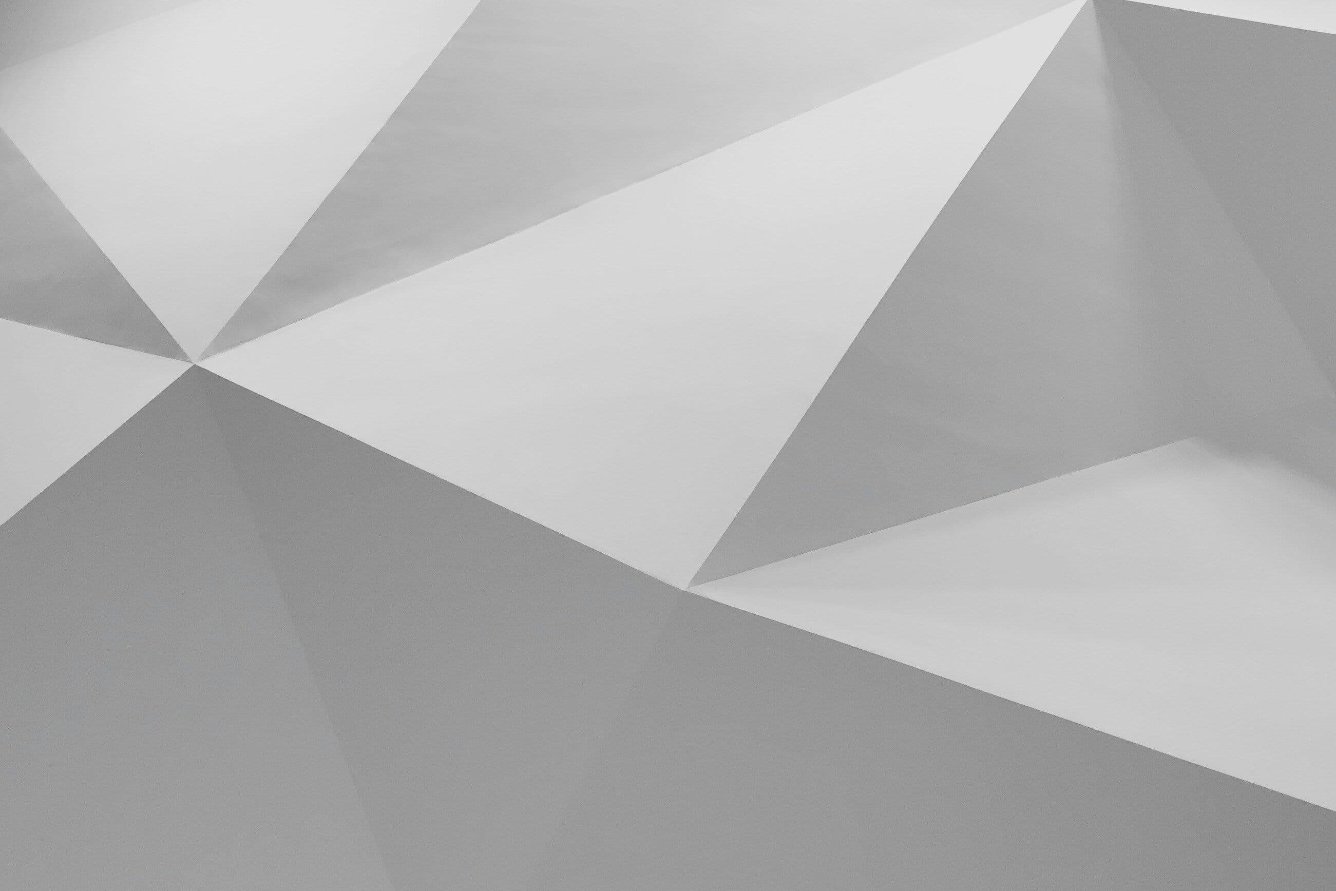 Abstract geometric pattern with overlapping triangular shapes in shades of gray, creating a modern, textured appearance.